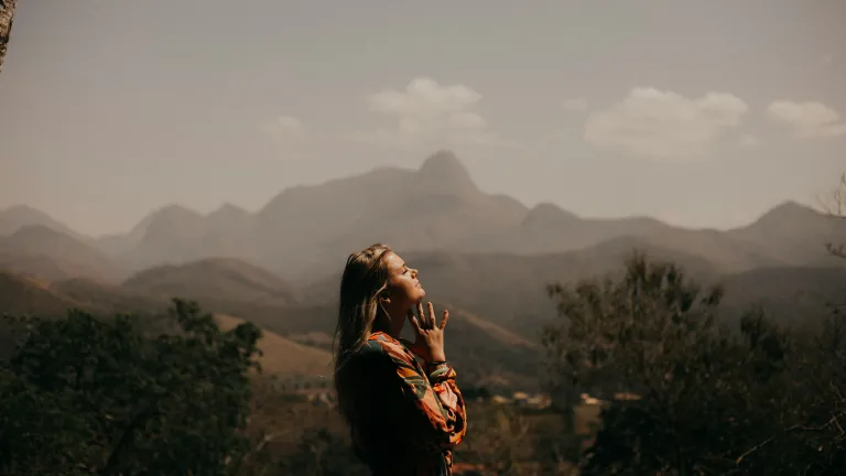 Meekness is a quiet power born in strength and involves emotions that are teachable, totally surrendered and responsive. a woman with folded hands standing outdoors amidst mountain scenary