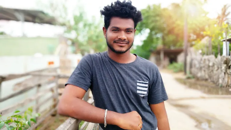 a smiling man standing outside with his arm leaning on a fence