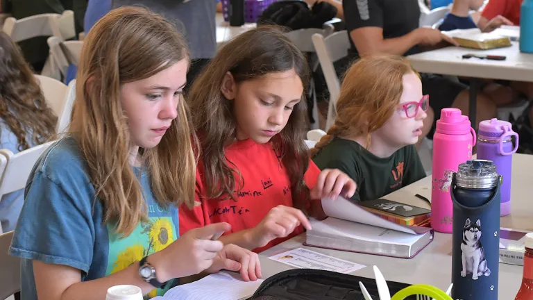 Camp Buckeye three little girls seated at a table with an open Bible and notebook