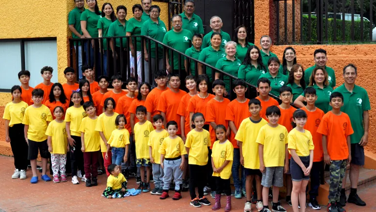 a large group of people standing outside, some lined up on a staircase, some in front of it, all wearing one of three colors of matching shirts