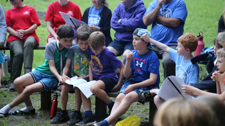 Camp Gilmont a group of people outdoors around a campfire, with a group of boys gathered around a song sheet
