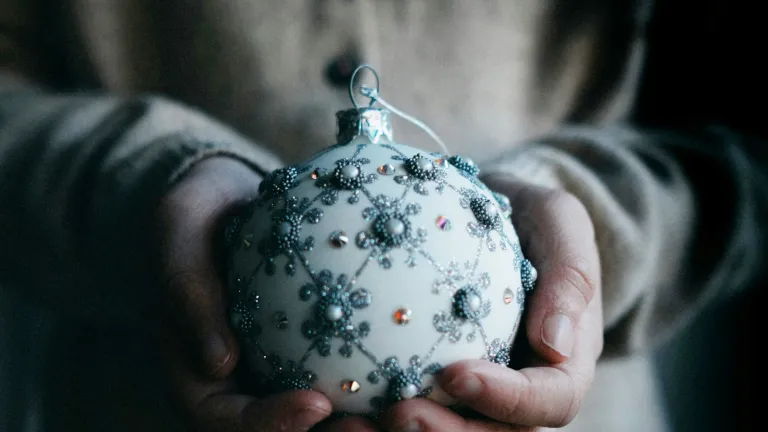 a woman holding a christmas ornament and wearing a seasonal sweater
