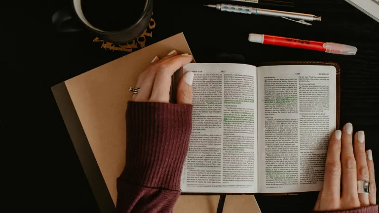 a woman's hands holding an open Bible with highlights in it