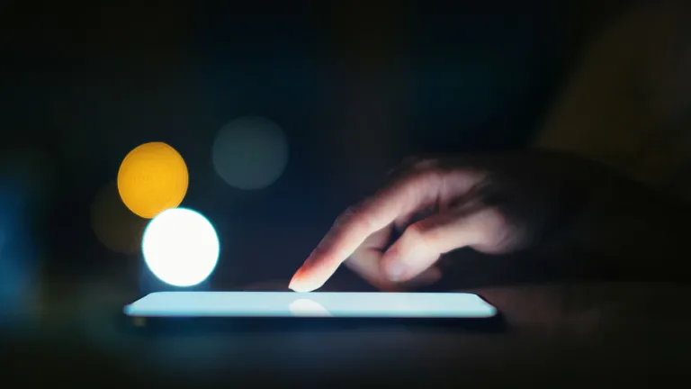 A finger touch the lit screen of an electronic device.