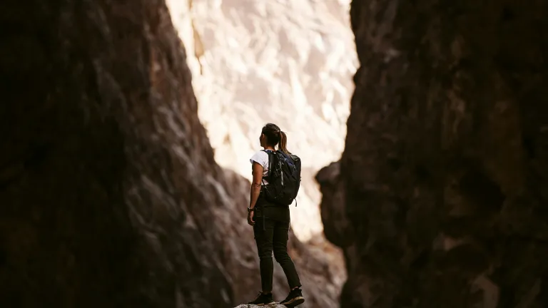 a woman with a backpack standing between two rockfaces