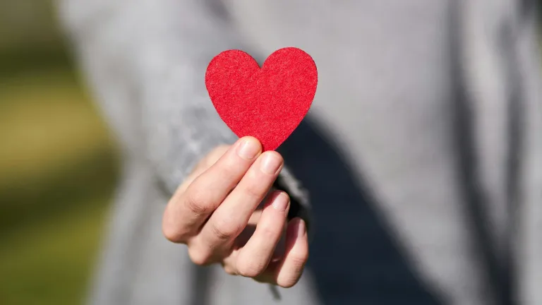 a woman's hand holding up a red paper heart
