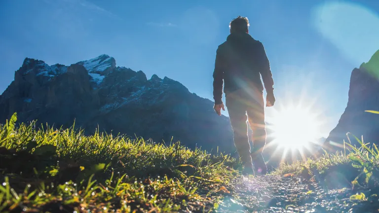 A person walking up a path with the sun in front of them.