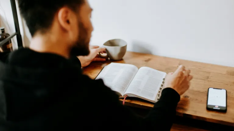 A man reading a Bible with his phone nearby.