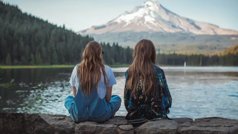 two women sitting on a ledge and looking at a lake