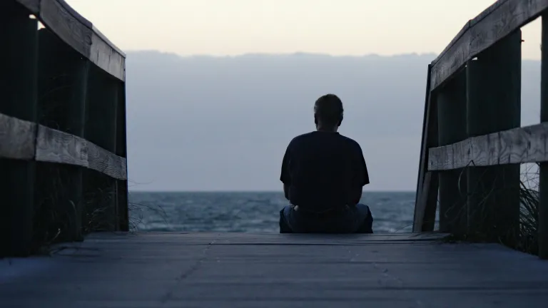 A person sitting at the end of a beach pier looking out at the water.