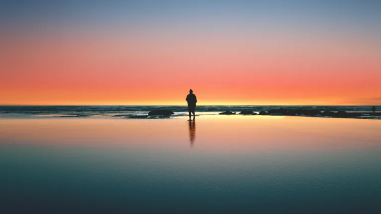 A calming image of a man silhouetted against a serene sunset on the beach