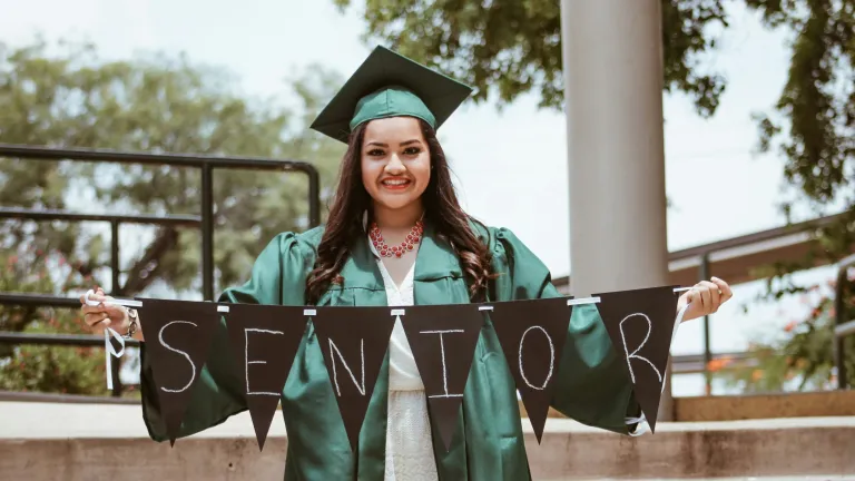 How you you prepare to make the most of your time in college? a young woman wearing a green graduation cap and gown while holding a banner that reads "senior."