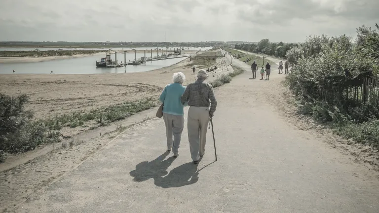 An elder couple walking together on a paved path.