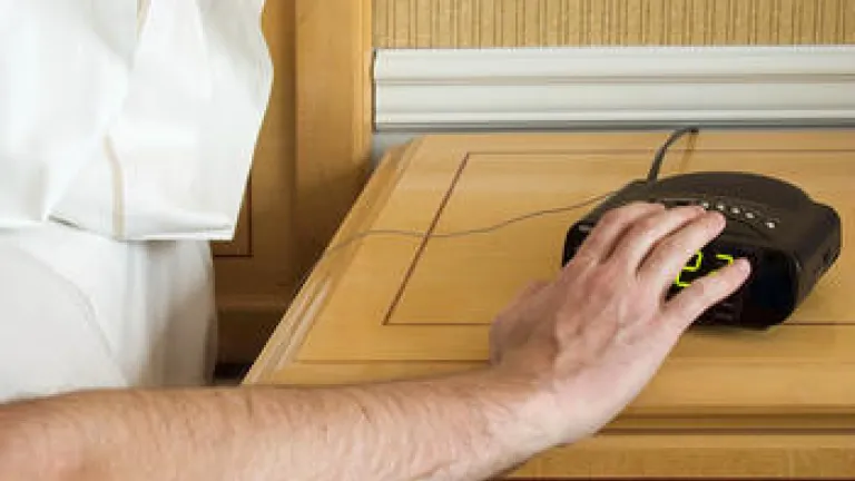 A man pressing the snooze button on an alarm clock.