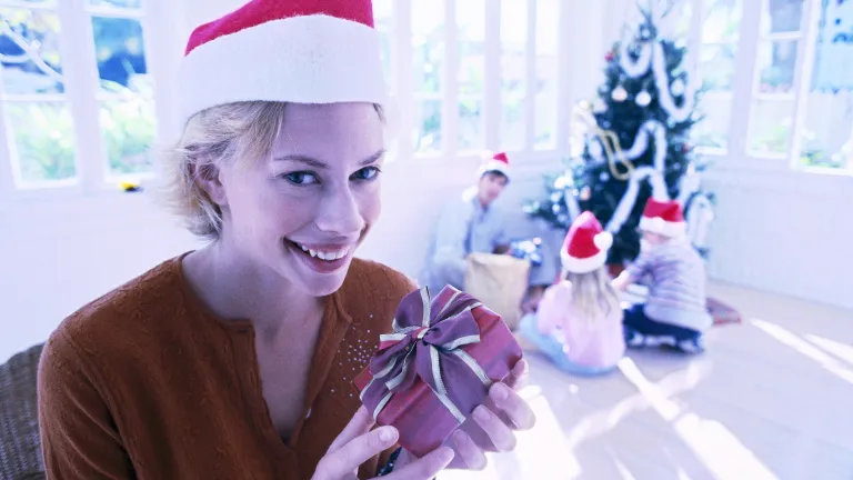 A woman wearing a red Santa hat and holding a gift.