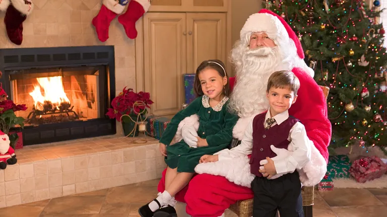 Two children sitting with Santa Claus in front of a Christmas tree.