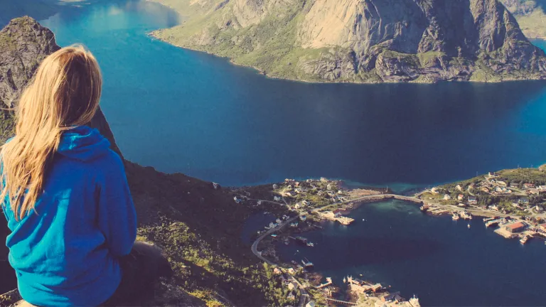 When the burden feels too great to bear and you are in danger of losing hope, take heart that hope remains alive because Jesus Christ is alive. A young woman on top of a mountain looking at a lake.