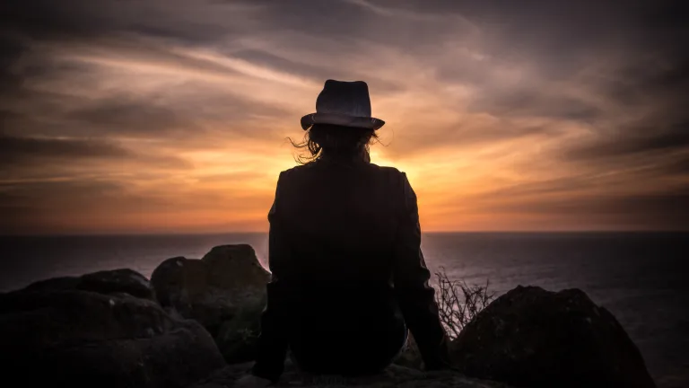 You might think it isn't a big deal and that you are only doing it for fun—after all it isn't hurting anyone, right? The problem is that it is hurting someone: you. A person sitting on a rock looking over water - orange sunset.