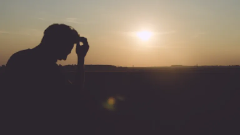 A man with head down as sun is setting.