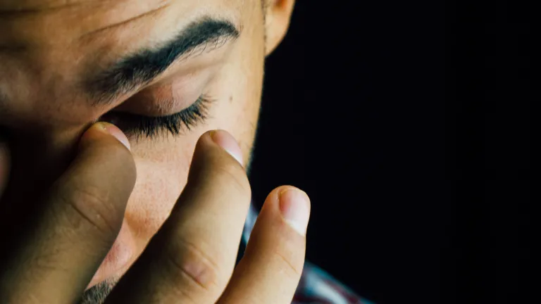 A young man holding his fingers over his eyes.