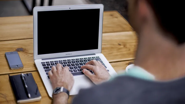 A man typing on a laptop while sitting a desk.