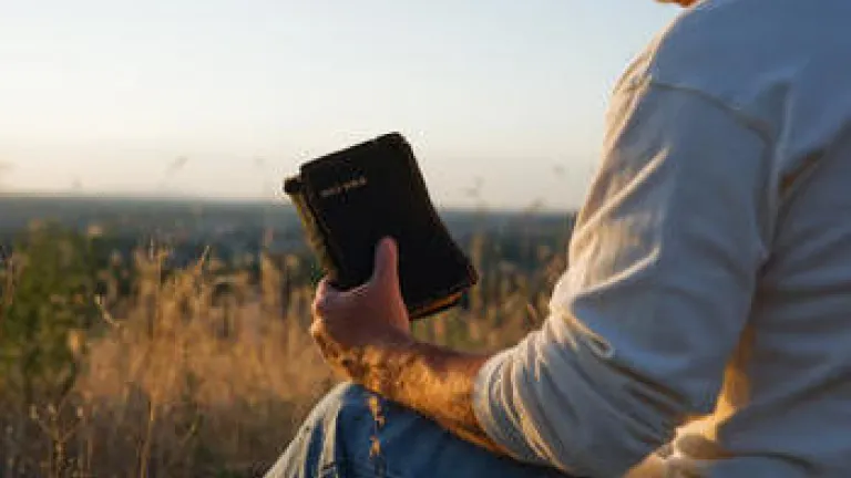 A man sitting on the ground holding an old Bible.
