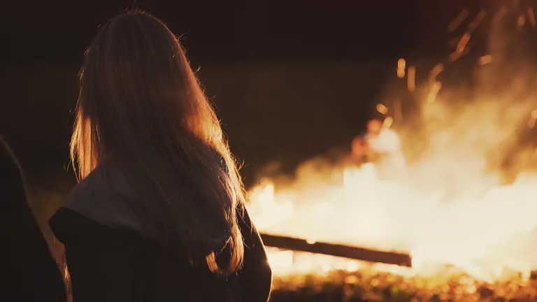 How about you? Are you at peace? A woman standing by a bonfire.