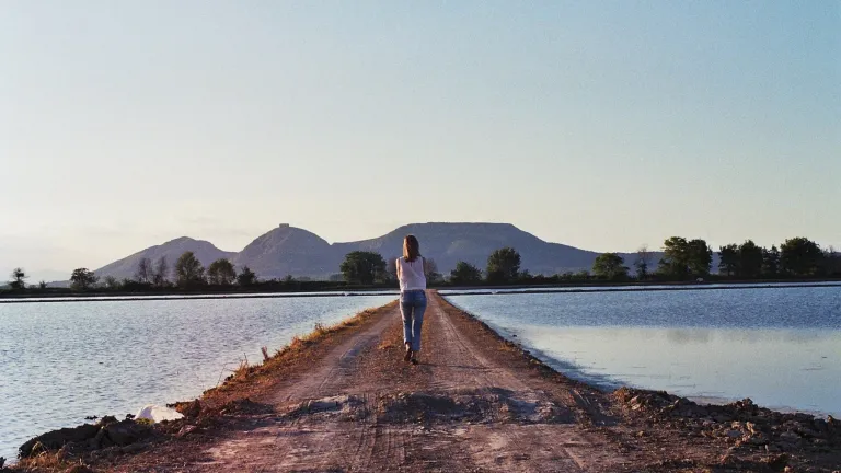A woman walking on a path between two bodies of water.
