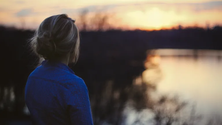 What is salvation? Why do we need it? A young woman looking at the sun setting over water.