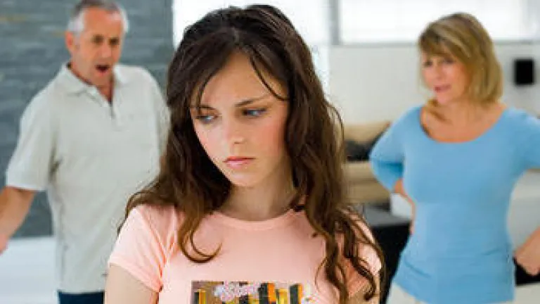 Teen girl in foreground with upset parents in background