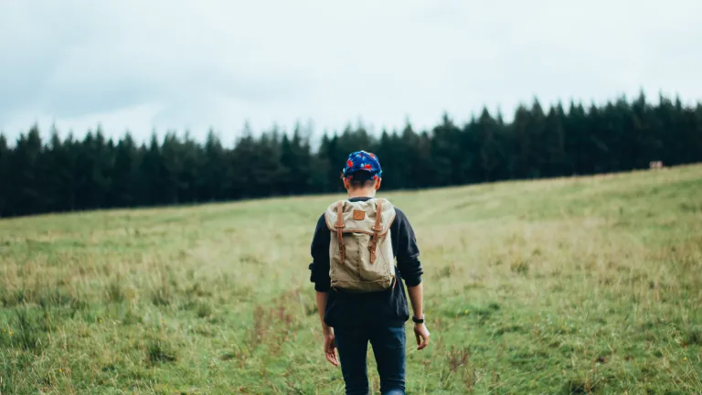 A young man walking up a hill with a backpack.