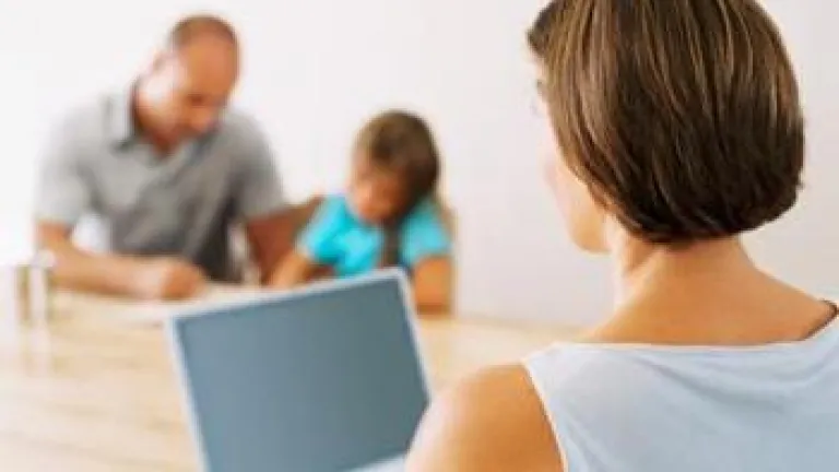 The Juggling Act Woman working on laptop with husband and child in background - The Juggling Act