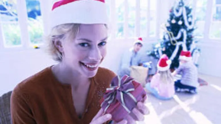 What's Behind the Magnetic Pull of the Christmas Season? A young woman holding a small present in front of Christmas tree.