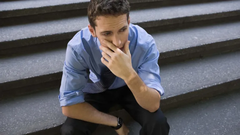 A young man sitting on concrete steps with his chin resting on his hands.