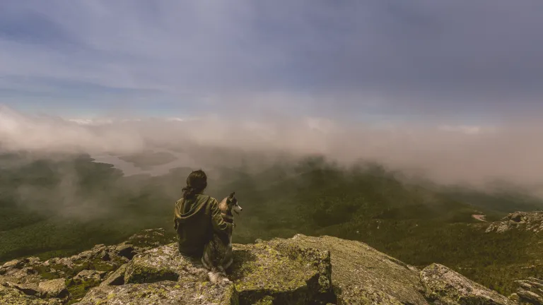 Even when we have unanswered prayers, know that God does listen. A woman sitting on cliff edge with her dog.