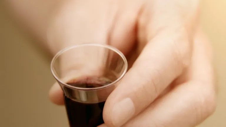 God had in mind that Jesus the Christ would initiate a new and wonderful experience of foot washing, bread and wine. These are the symbols of the triumph of God’s master plan for saving man from death. A man holding a small clear cup of wine.