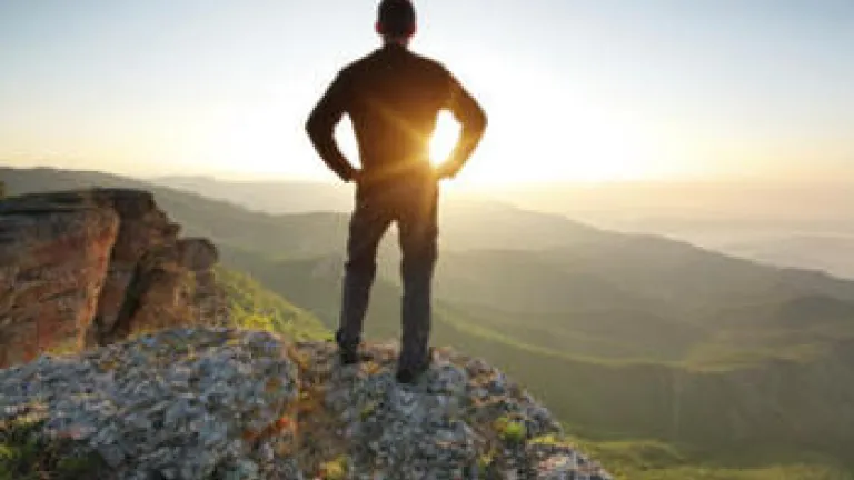 A young man standing at the edge of cliff looking at the setting sun.