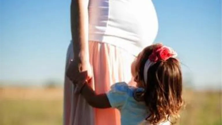 A young child holding a pregnant woman's hand.