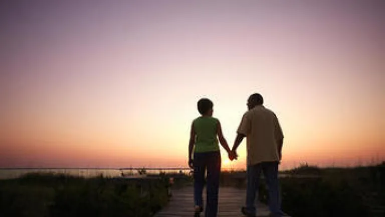 An older couple walking on a board walk while sun is setting.