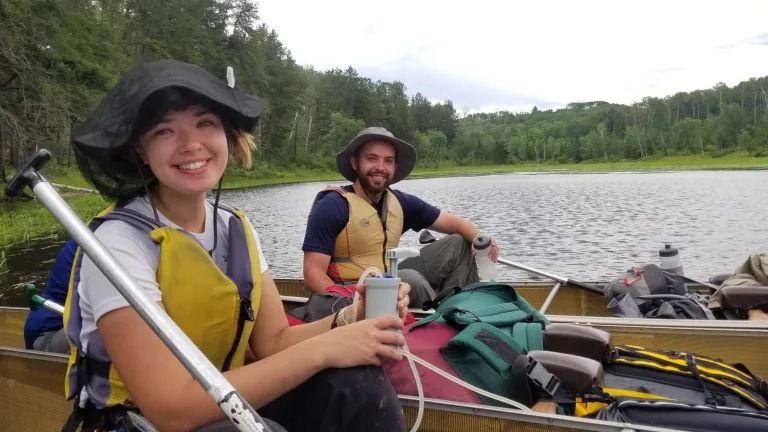 Two campers filter drinking water from the lake using a pump.