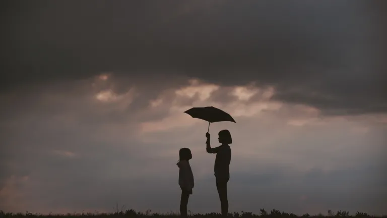 Photo of a girl holding an umbrella over another girl.