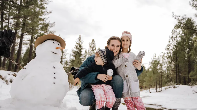 a woman hugging a boy and a girl as they stand beside a snowman