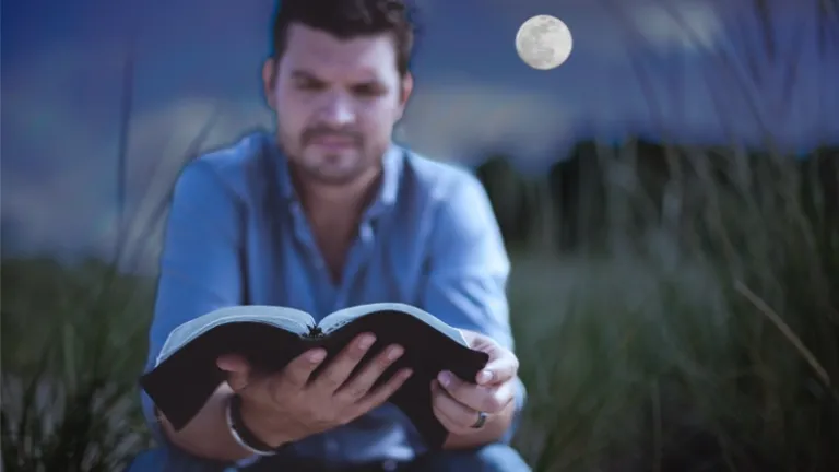 A man reading a Bible in the light of a full moon