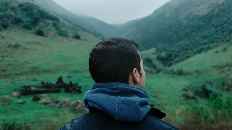a man looks towards a mountain landscape that slopes up both to the right and to the left