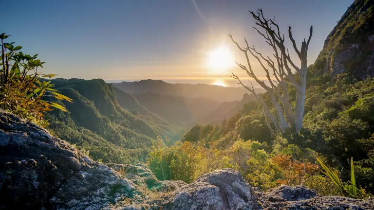 a mountainous landscape with the sun setting in the background over the water