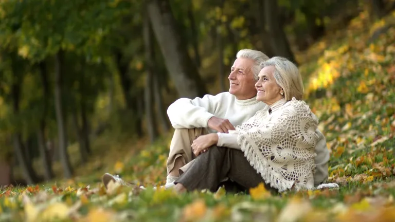 an older couple sitting outdoors amongst the leaves and trees