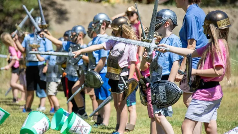 a group of children wearing pretend armor and holding plastic swords standing outdoors