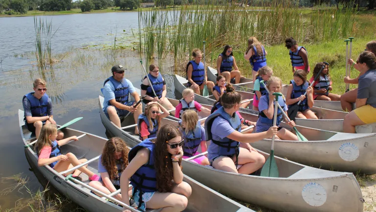 a group of preteen campers and staff sitting in canoes