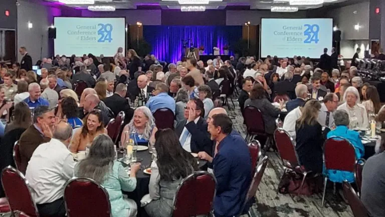 a large group of people seated indoors around circular tables