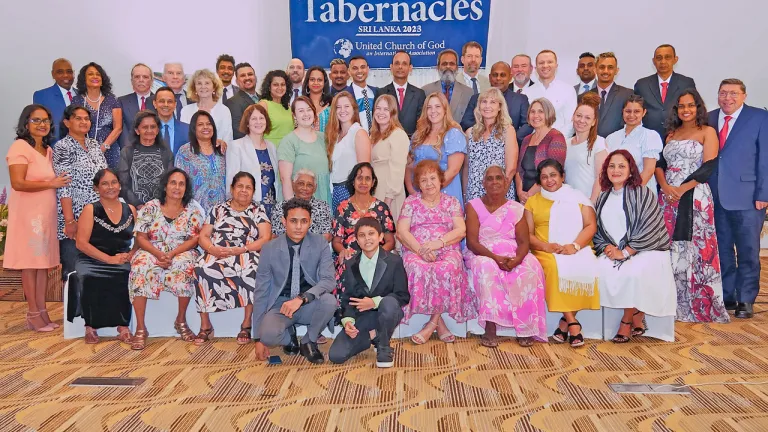 A group of people standing indoors under a Feast of Tabernacles banner